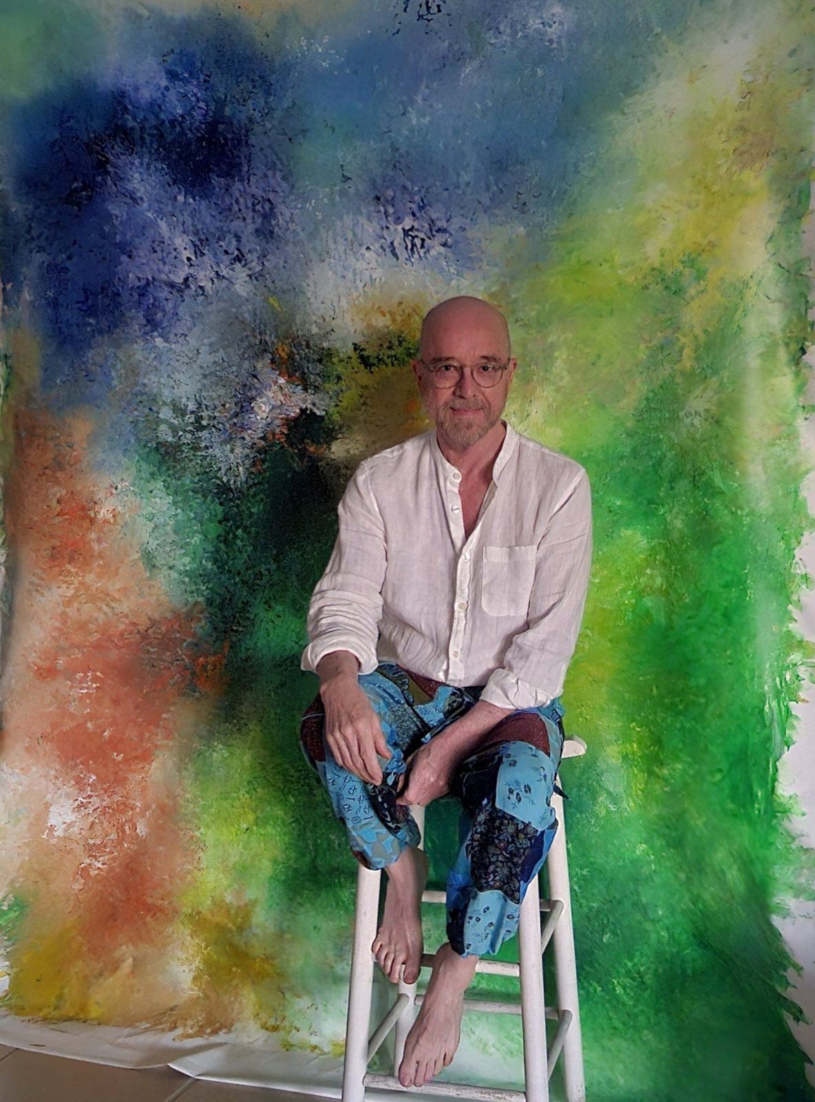 Dr. Enzo Trapani seated in his studio in front of one of his paintings